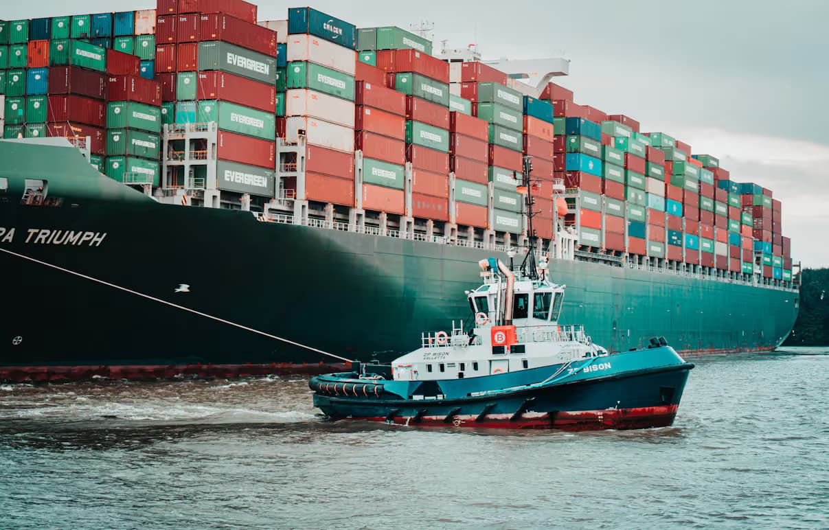 “A tugboat guiding a fully loaded container ship stacked high with shipping containers”