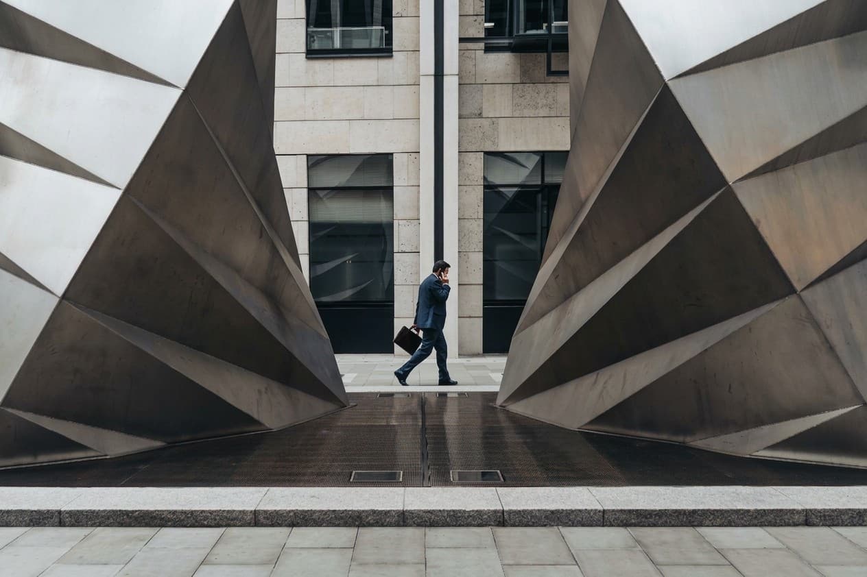 A businessman on the phone walks past two large angular steel sculptures in a city plaza